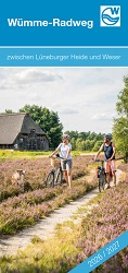 Titelseite des Flyers Wümme-Radweg, auf dem eine blühende Heidelandschaft zu sehen ist, durch die ein Weg führt. Im Hintergrund ist ein alter landwirtschaftlicher Hof zu sehen, im Vordergrund stehen zwei Radfahrer mit ihrem Hund.